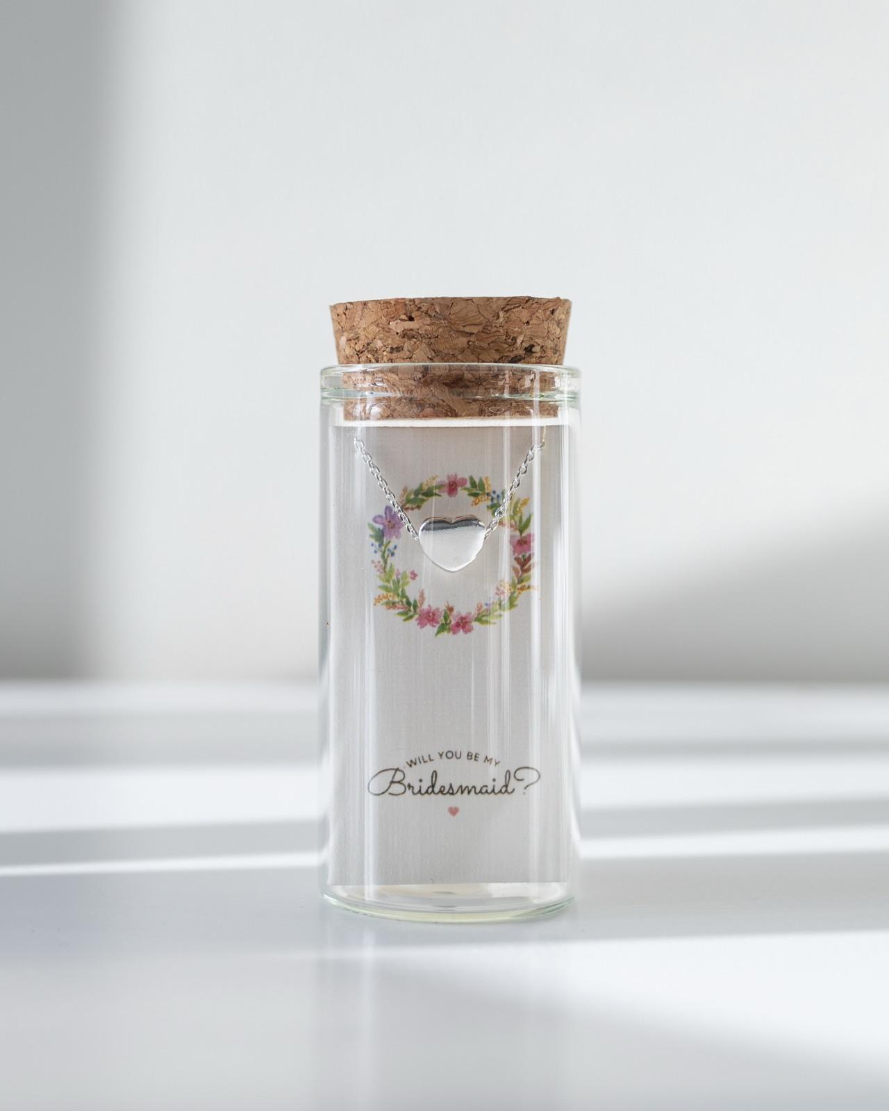 A heart necklace in its bottle with a bridesmaid card