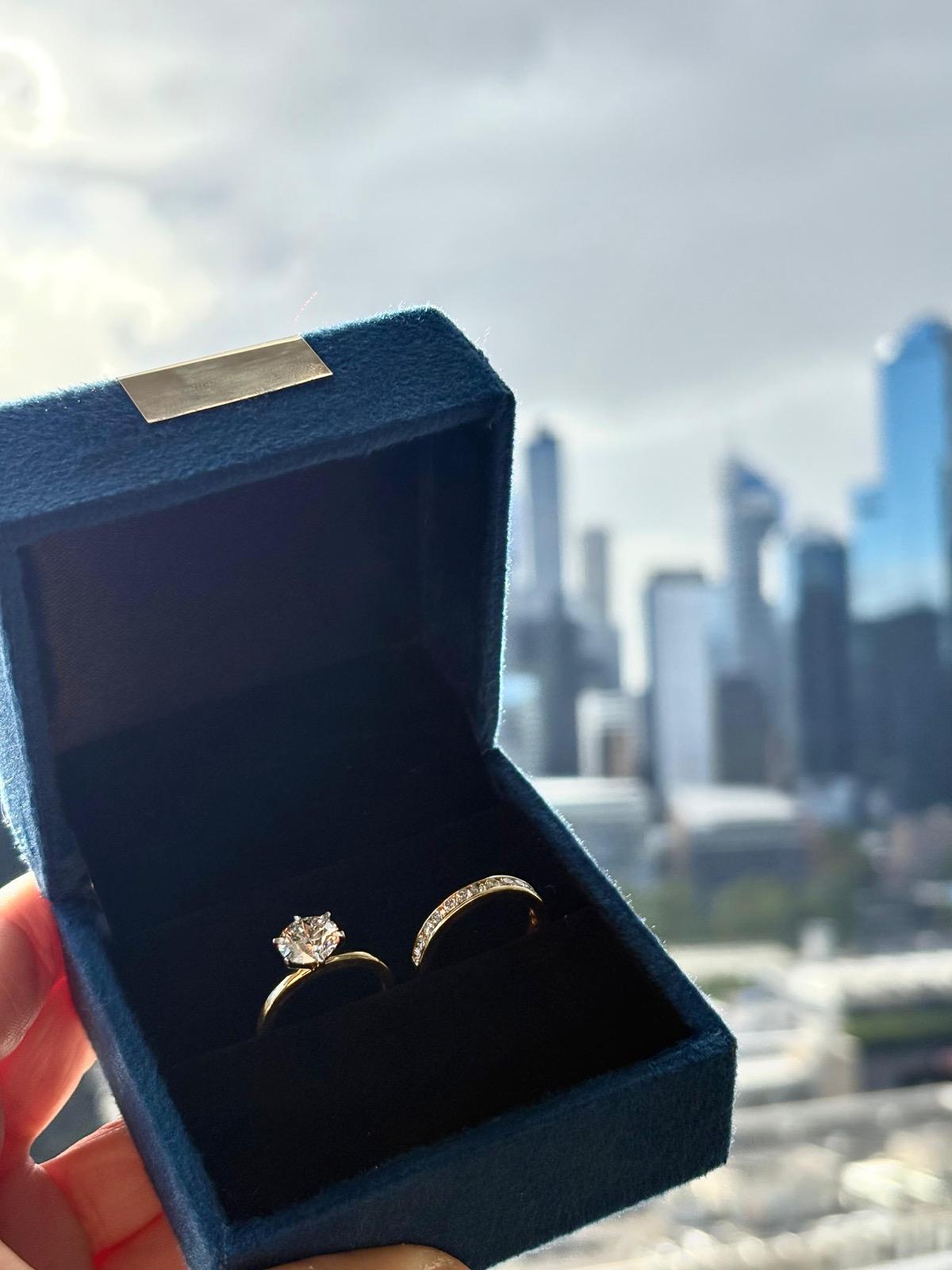 An engagement ring and its matching band in an ARKH box, the Melbourne skyline behind