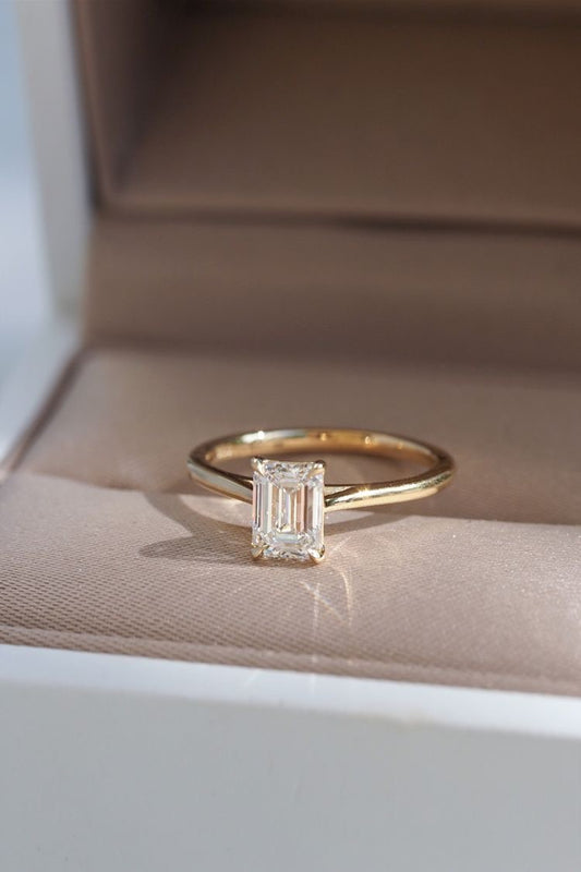 Gold ring with a diamond on a beige cushion in an open jewelry box.