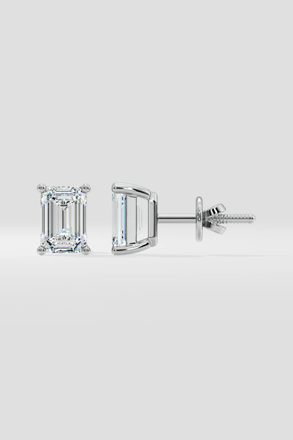 The EMERALD SOLITAIRE EARRINGS are a pair of emerald-cut lab-grown diamond studs with VS2 clarity, set in white metal prongs and displayed from the front and side on a plain light gray background.