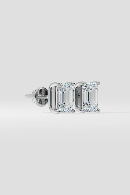 The EMERALD SOLITAIRE EARRINGS are lab-grown, emerald-cut diamond studs with VS2 clarity set in silver prongs, shown on a light gray background.
