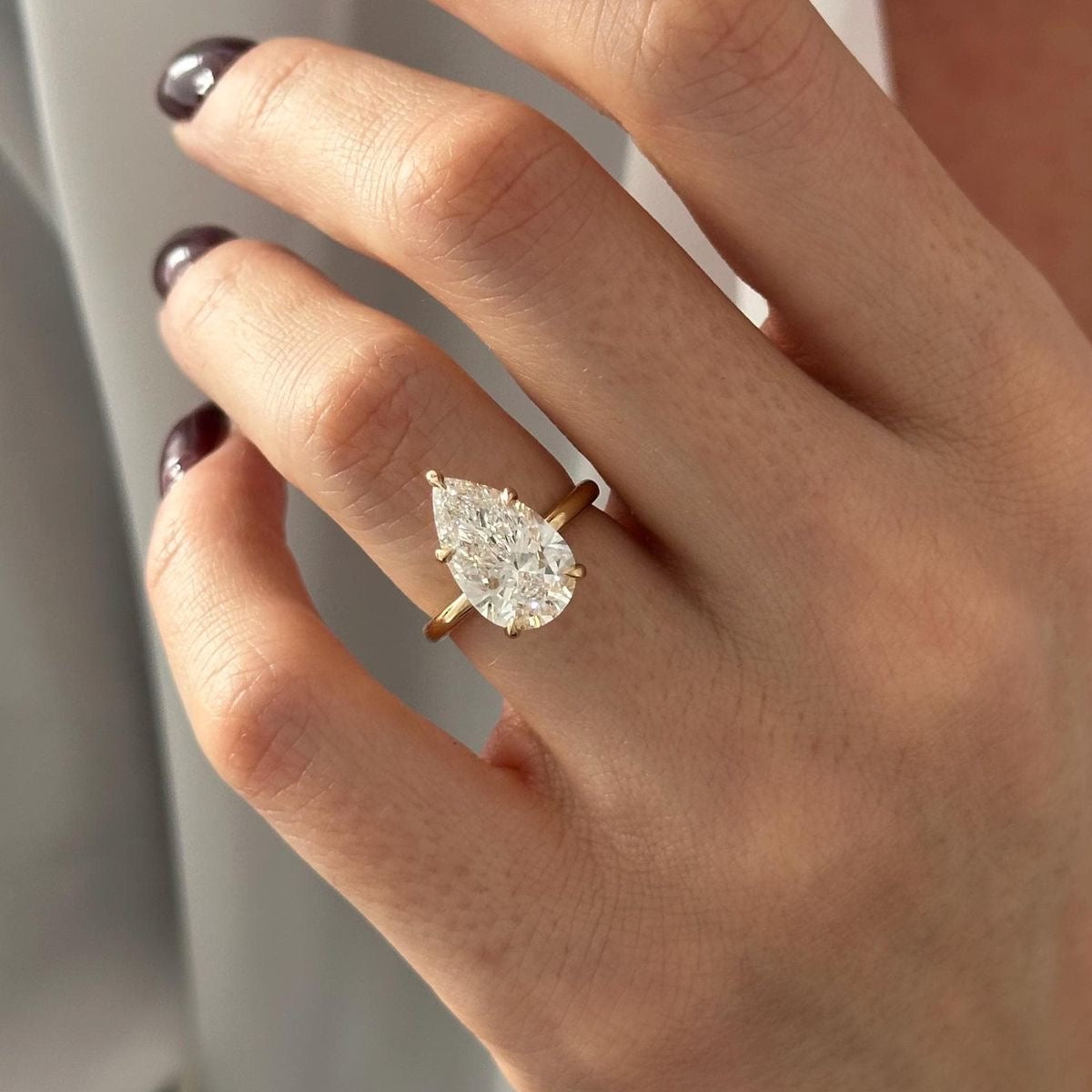 Pear solitaire ring in gold worn on hand showing scale and sparkle