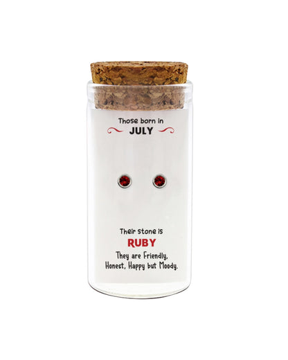 Jar with cork lid containing ruby gemstone earrings, labeled for July birthstones.