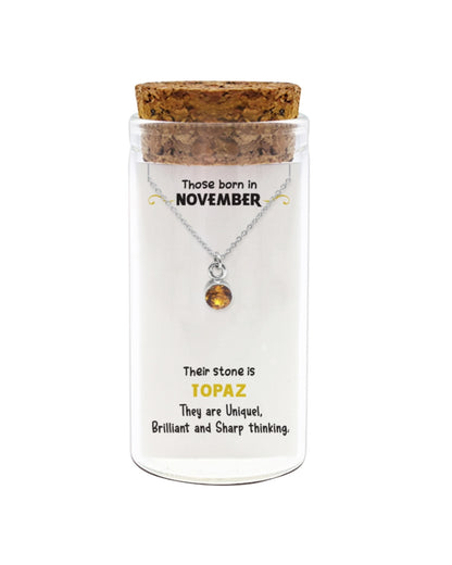 Necklace with a topaz stone in a glass jar with a cork lid, featuring information about those born in November.