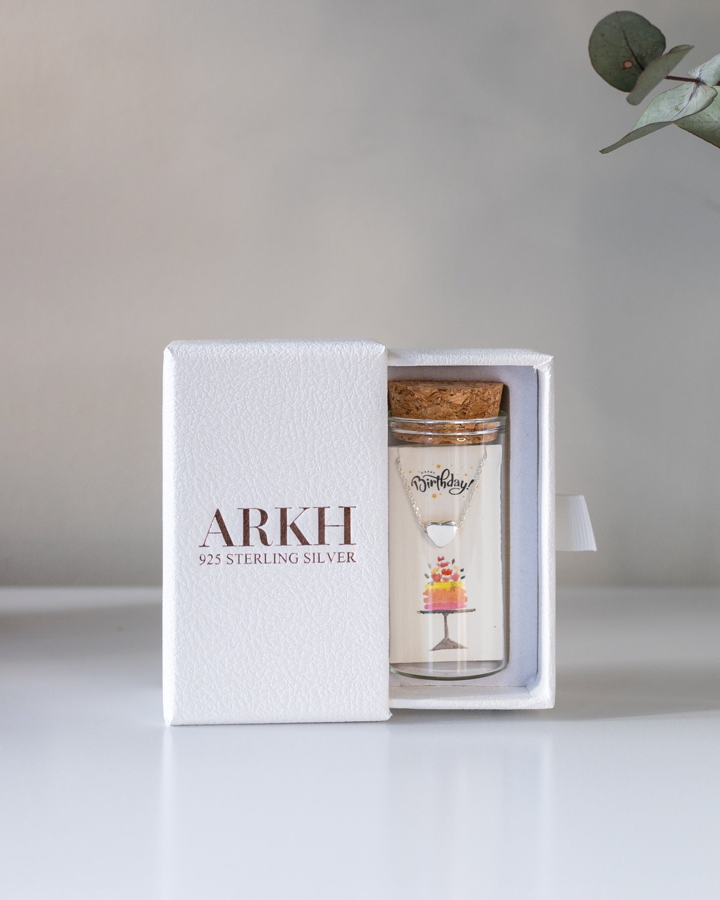 Glass jar with cork lid containing birthday heart necklace with cake art – ready-to-gift jewelry