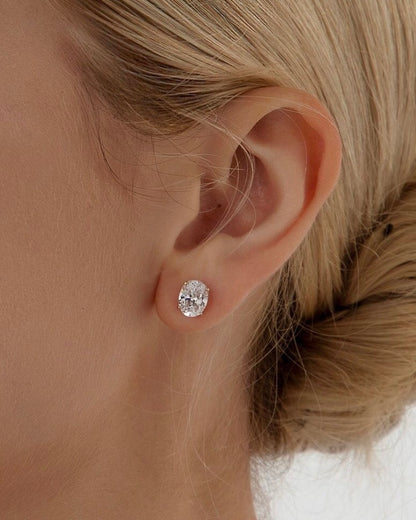 Close-up of oval solitaire earring worn on ear – elegant gold oval diamond studs