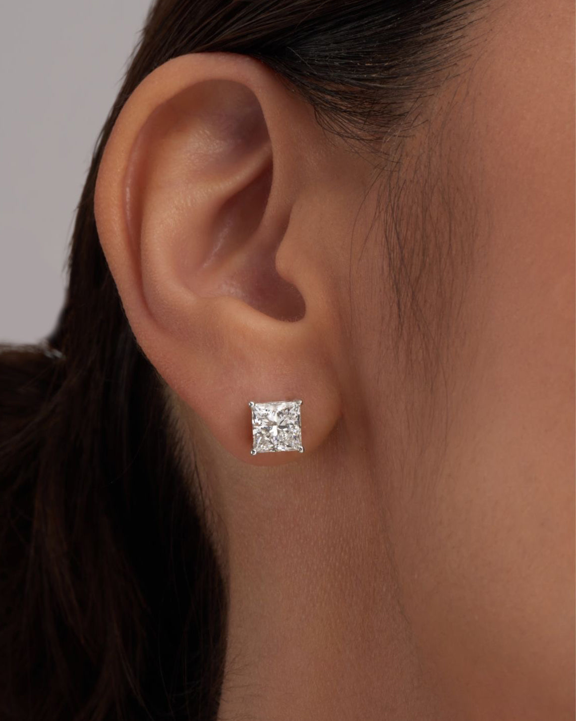Close-up of princess solitaire earring worn on ear – elegant gold princess diamond studs
